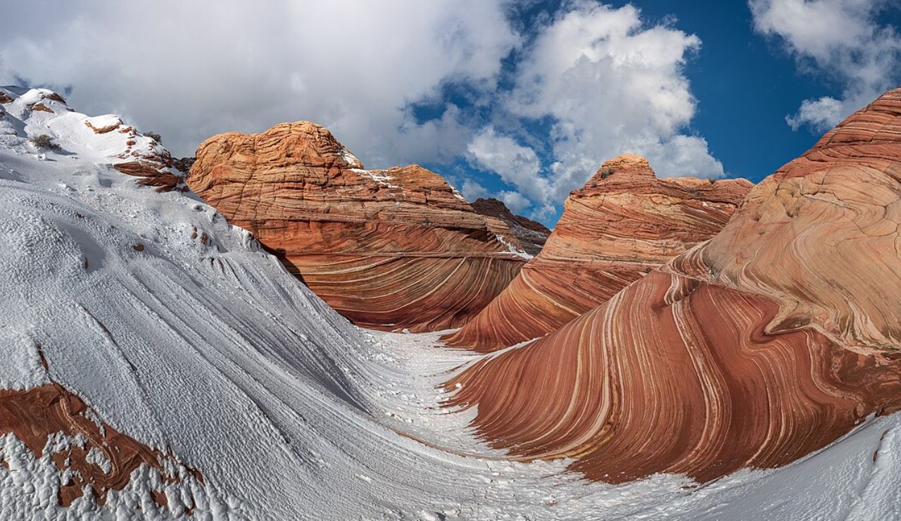 Snow-covered red sandstone formations at The Wave in Arizona’s Coyote Buttes North, showcasing dramatic swirls and layered rock under a partly cloudy sky.