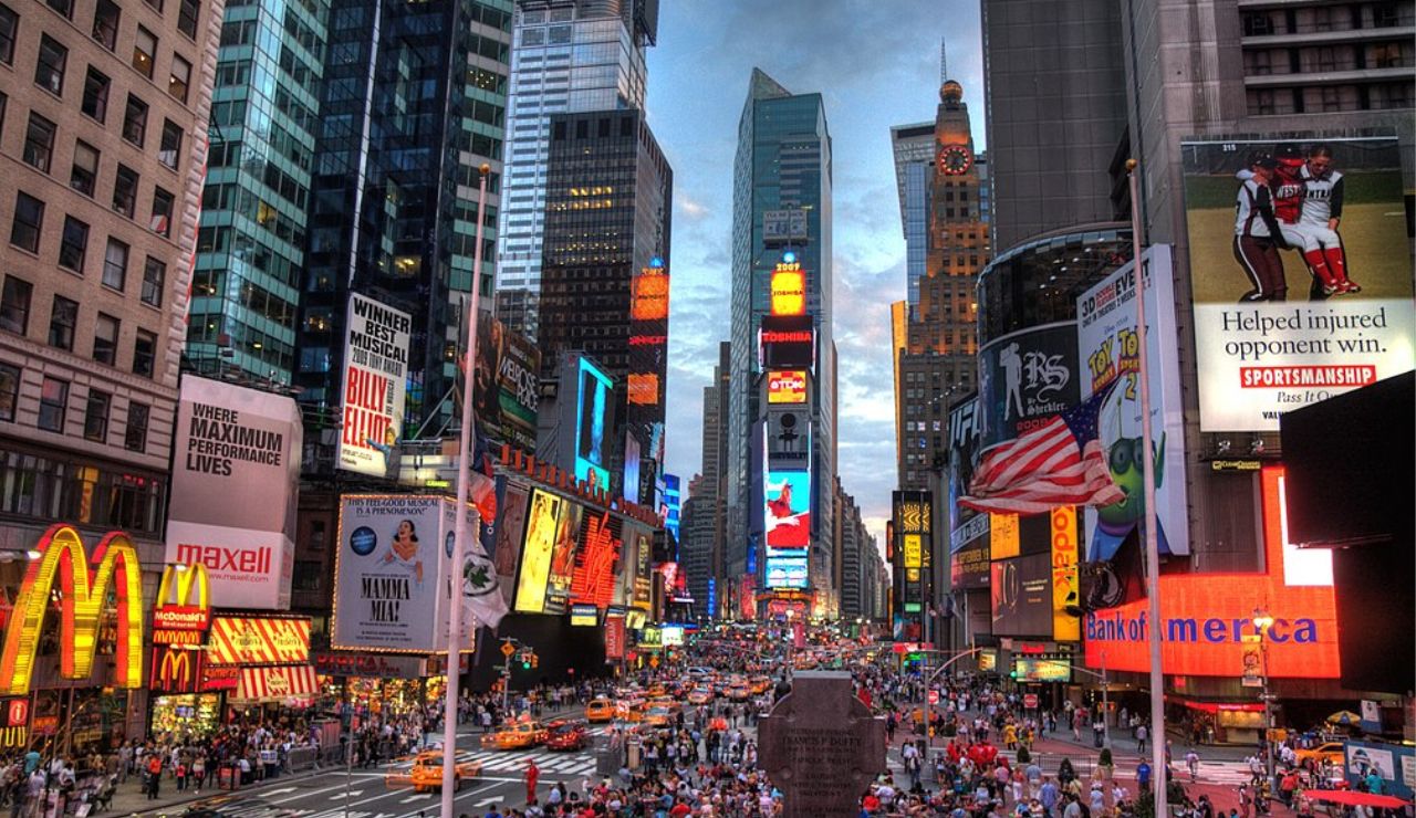 Times Square in New York City at dusk, filled with bright billboards, bustling crowds, and yellow taxis