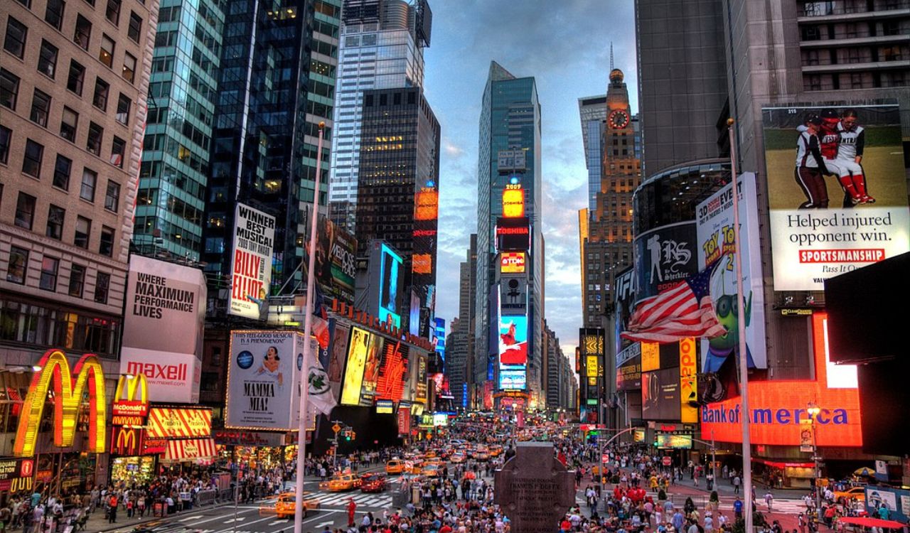 Crowded city square glowing with bright lights and tall buildings.