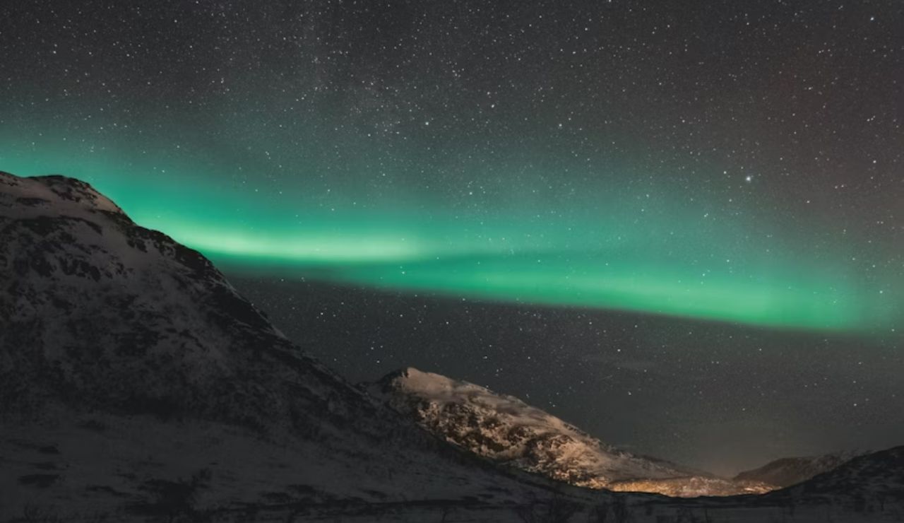 Aurora Borealis stretching across the starry night sky above snow-covered mountains in Tromsø, Norway.
