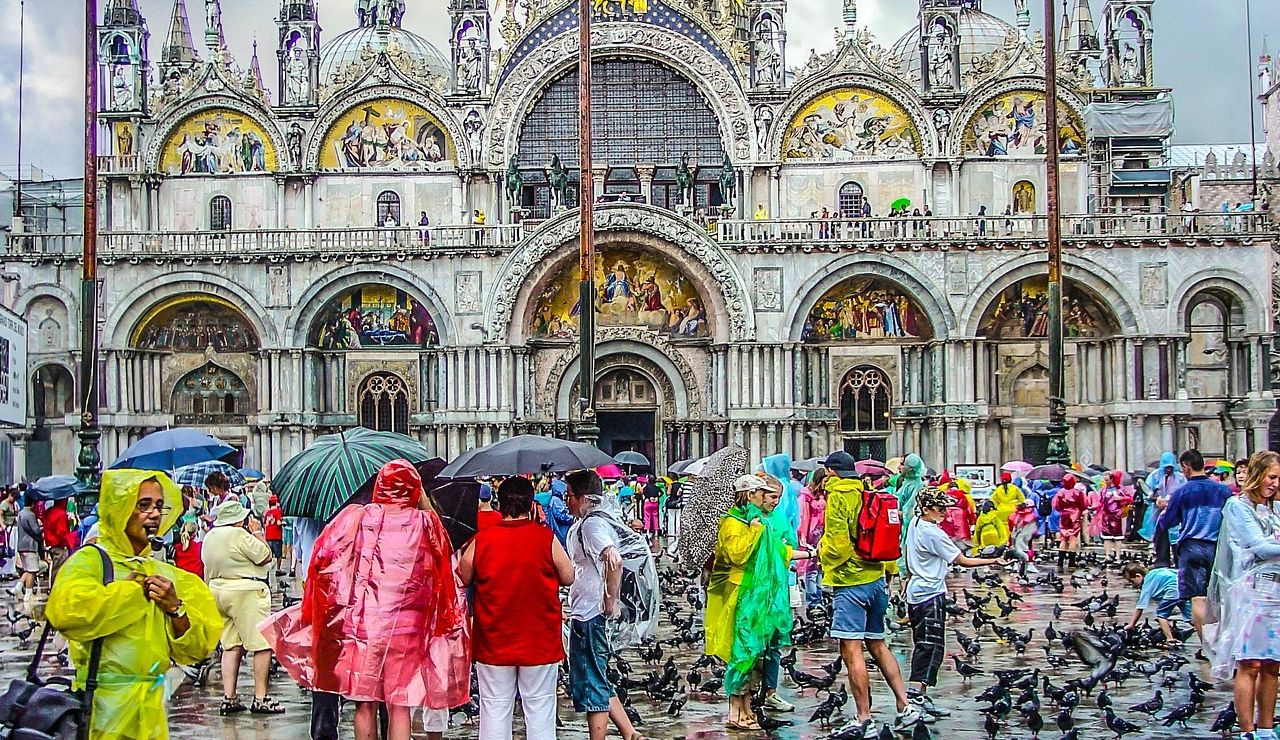 Tourists in colorful raincoats gather in front of St. Mark's Basilica in Venice on a rainy day.