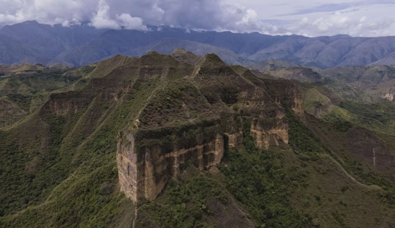 Aerial view of the rugged green mountains and dramatic cliffs in Vilcabamba, Ecuador, with the Andes in the background under a cloudy sky.