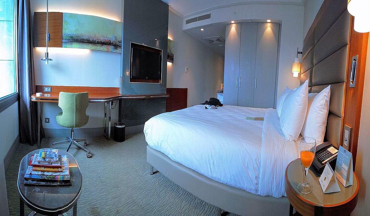 A stylish hotel room featuring a large, plush bed, a sleek work desk, flat-screen TV, and cozy lighting—perfect for relaxing or catching up on work.