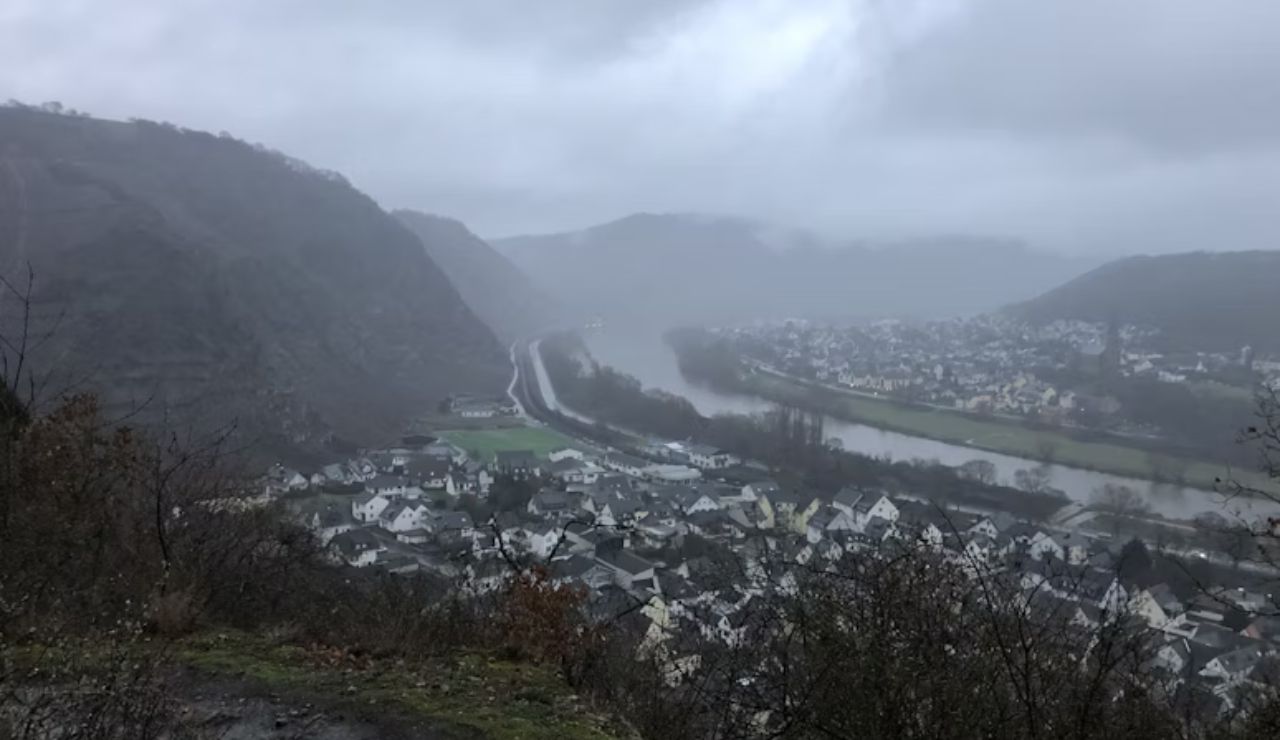 Foggy view of a riverside village nestled between hills on a rainy day.