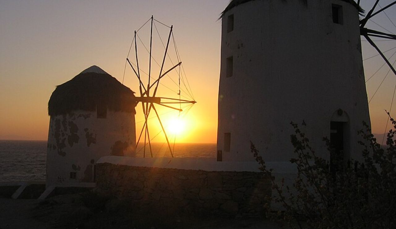 Traditional Mykonos windmills silhouetted against a golden Aegean sunset.