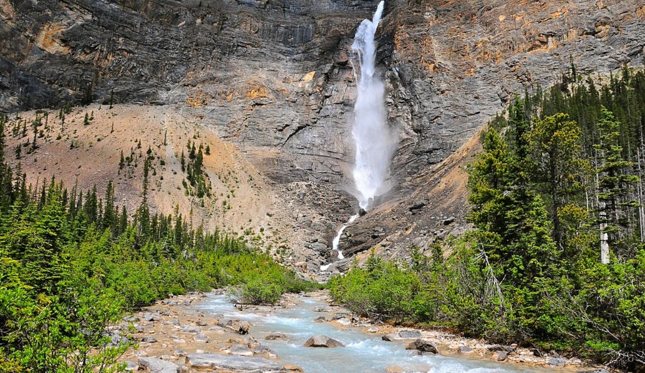 Tall waterfall cascading down a rocky cliff into a turquoise stream at Takakkaw Falls in Yoho National Park, British Columbia, Canada.