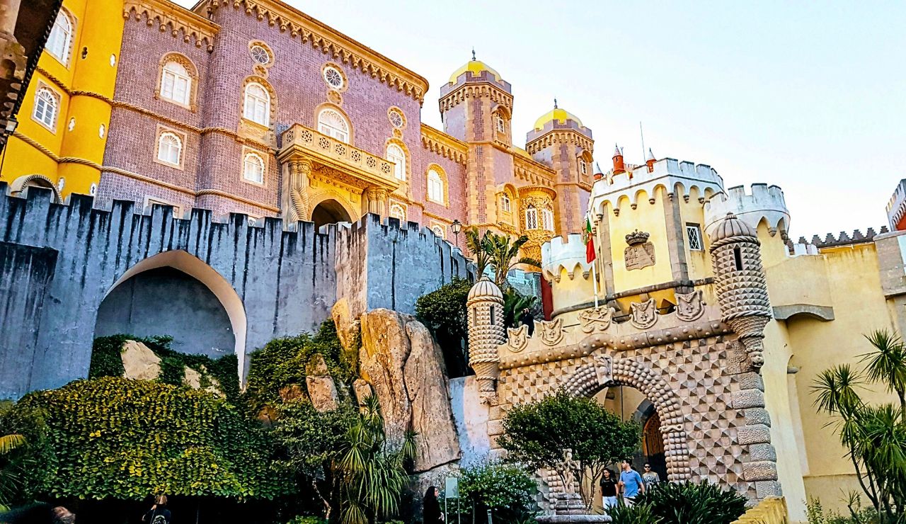 Pena Palace in Sintra, Portugal, features colorful exteriors, ornate towers, arched entryways, stone walls, and lush greenery.