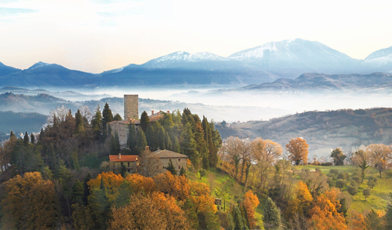 Castello di Petroia nestled in autumn trees with mountains in Umbria, Italy.