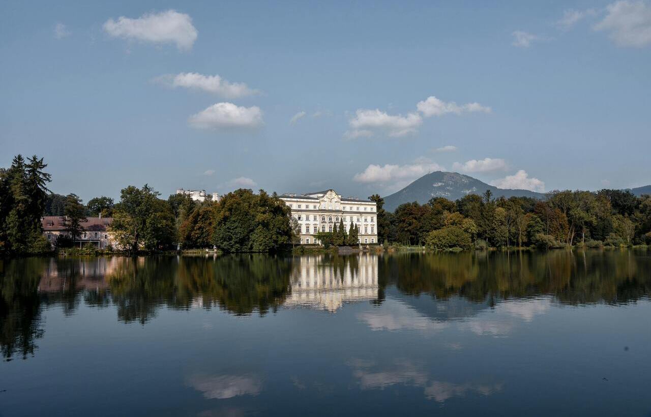 Schloss Leopoldskron reflected in lake with mountain backdrop in Salzburg.