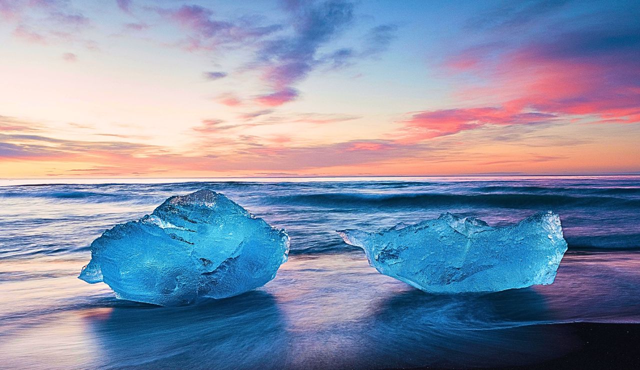 Ice chunks sparkling on the black-sand beach at sunrise with soft golden light.