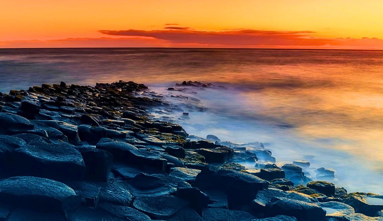 Basalt hexagonal columns descending into the sea with dramatic clouds overhead.