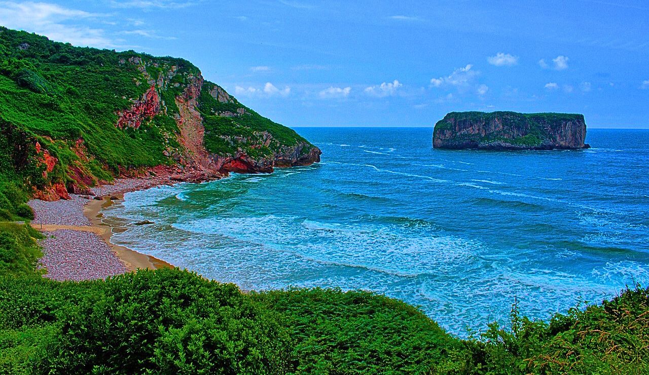 A small inland beach with gentle waves and green meadows surrounding the cove.