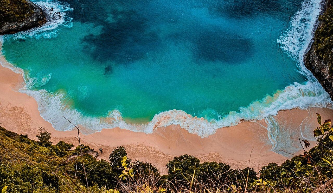 Gentle pink-tinted shoreline meeting calm, turquoise water under a pastel sunset.
