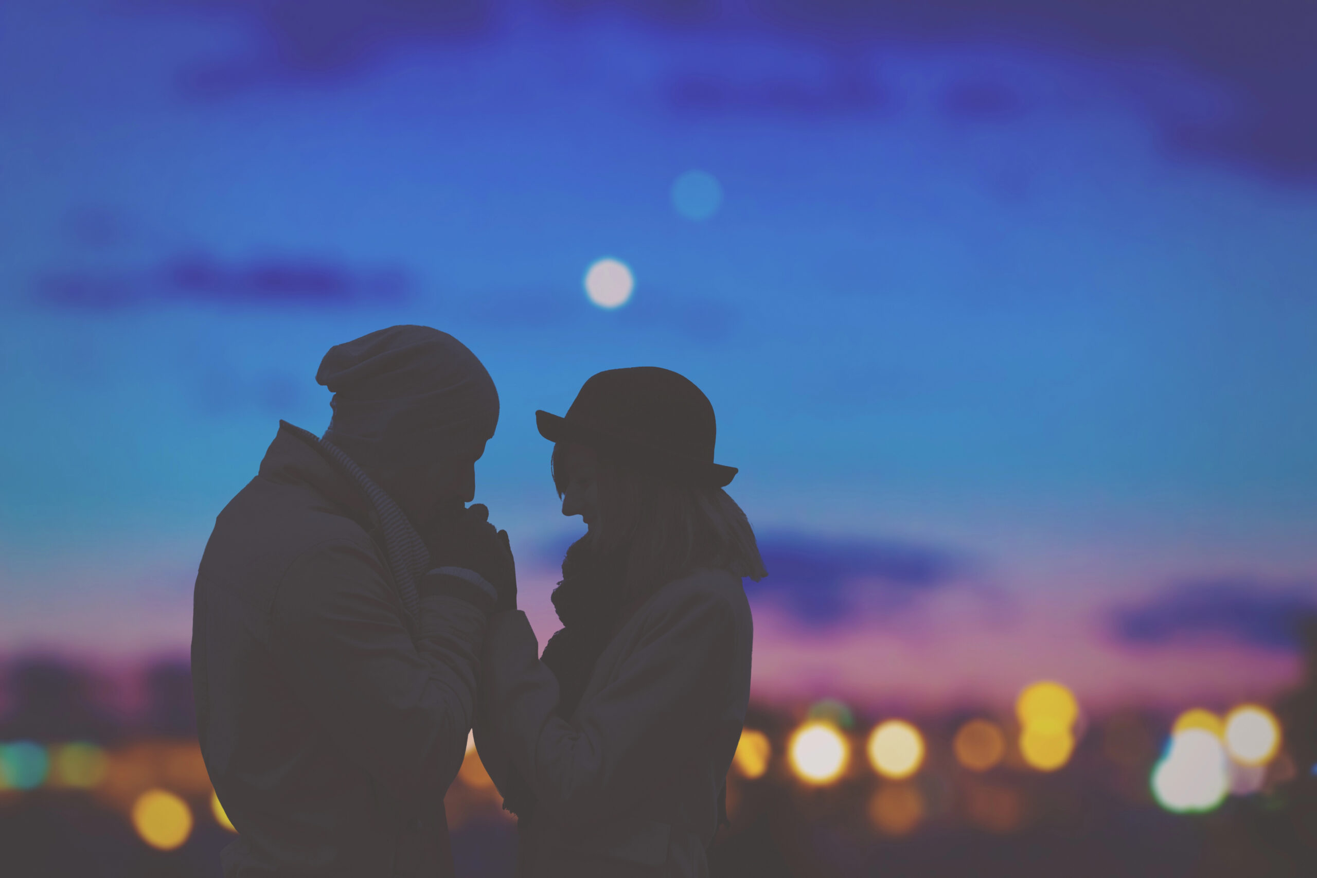 Silhouette of couple at dusk in front of city lights and a blue night sky.