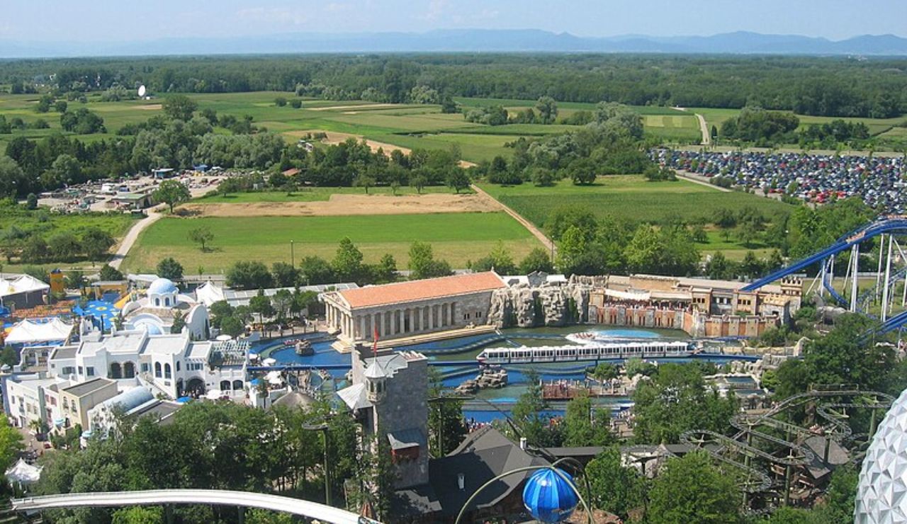 Aerial view of Europa-Park in Germany, showing themed buildings, a roller coaster, water ride, and surrounding countryside.