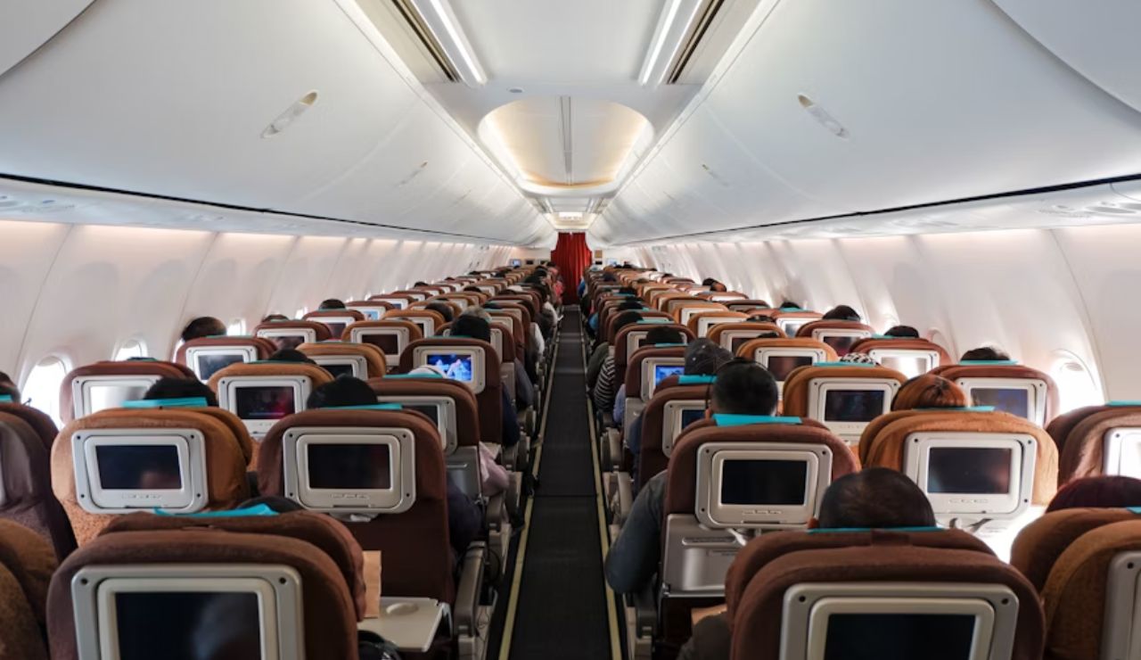 Passengers seated inside a commercial airplane with seatback screens.