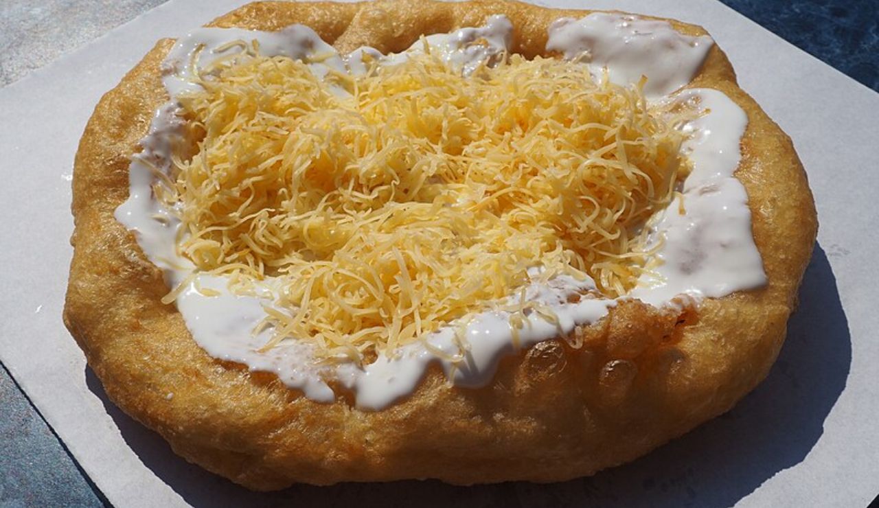 Hungarian lángos topped with sour cream and shredded cheese.