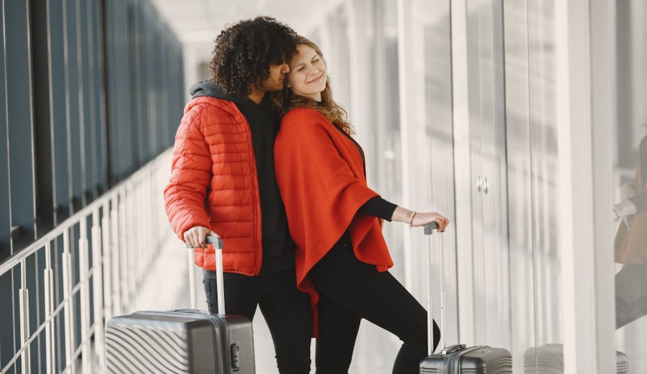 Happy couple in matching red outerwear standing with luggage in an airport hallway.