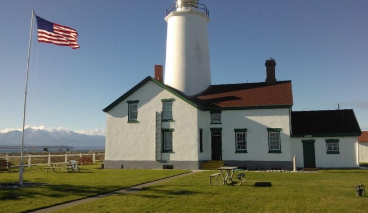 New Dungeness Lighthouse in Washington with an American flag and mountain backdrop.