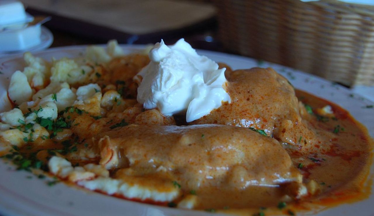 Chicken paprikash served with nokedli dumplings, topped with a dollop of sour cream and garnished with chopped parsley.