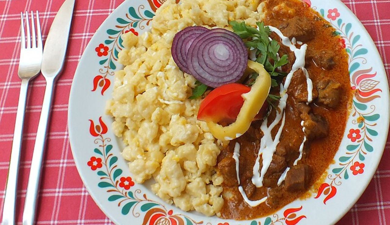 Hungarian beef stew with nokedli dumplings, garnished with onions and peppers.