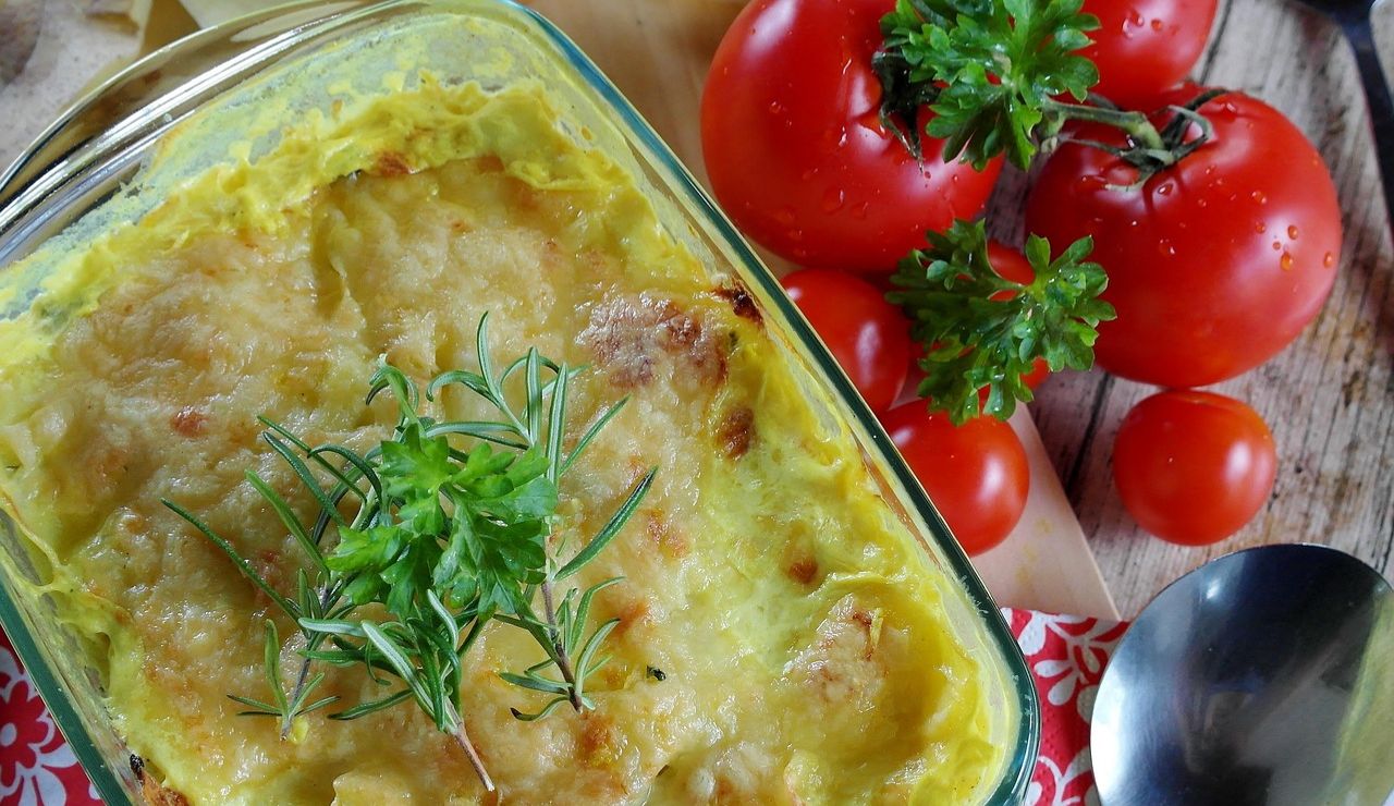 Hungarian layered potato casserole (Rakott Krumpli) topped with herbs, surrounded by fresh tomatoes and potatoes.