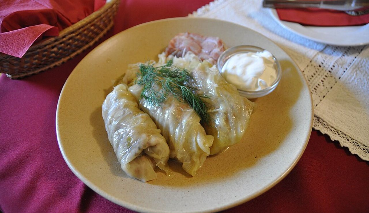 Töltött káposzta, traditional Hungarian stuffed cabbage rolls served with sour cream and fresh dill on a beige plate.