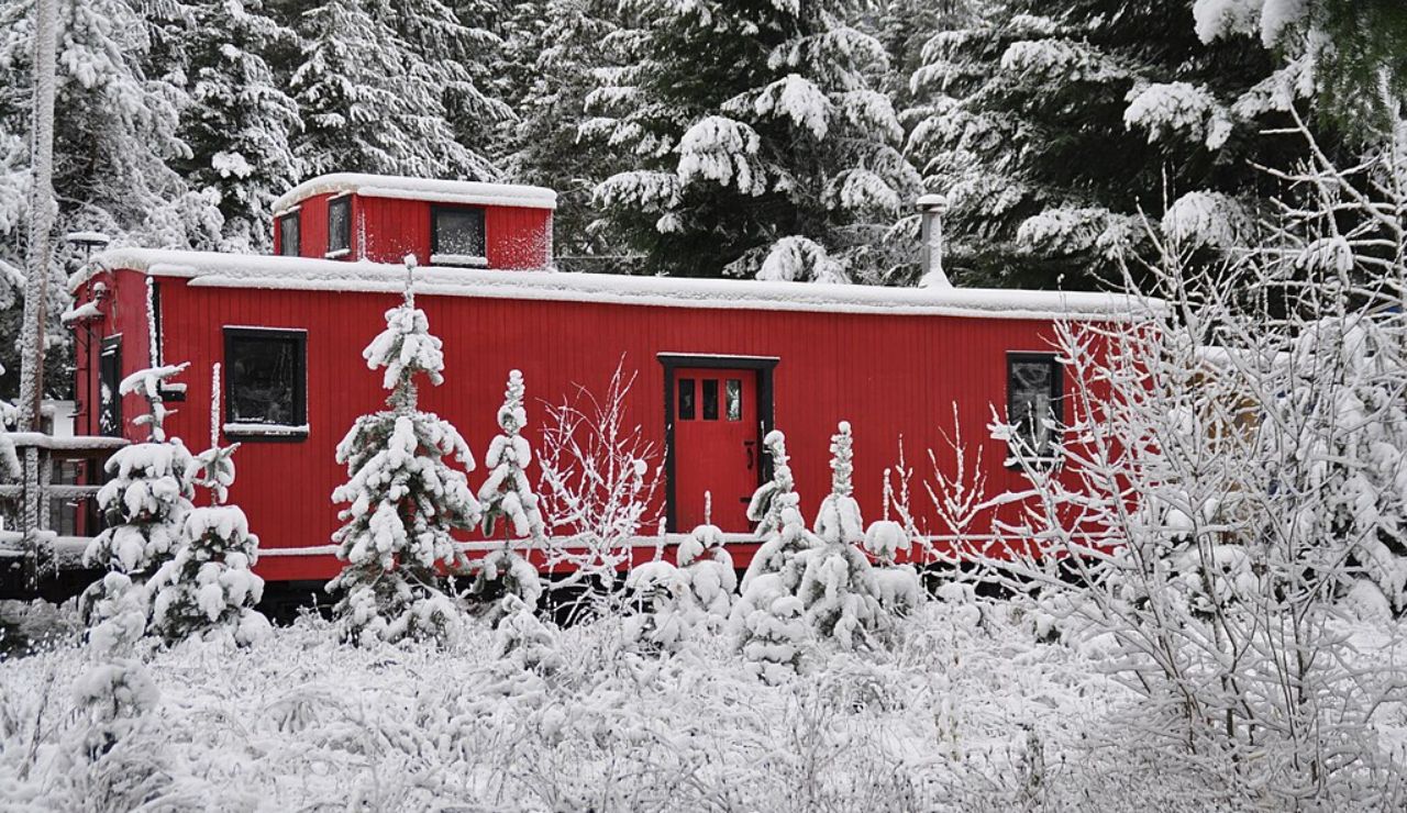 A bright red cabin-style railcar surrounded by snow-covered trees in a winter forest setting.