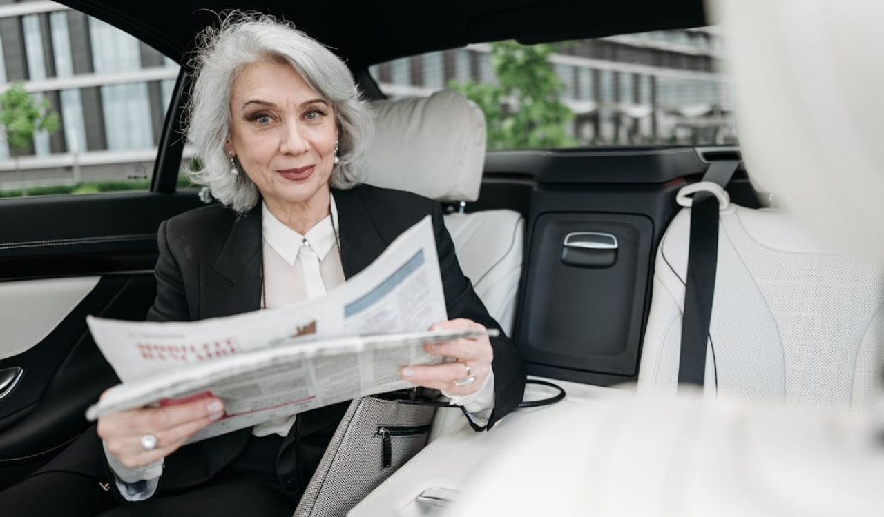 Confident senior woman reading a newspaper in a luxury car, symbolizing peace of mind that comes with having travel insurance