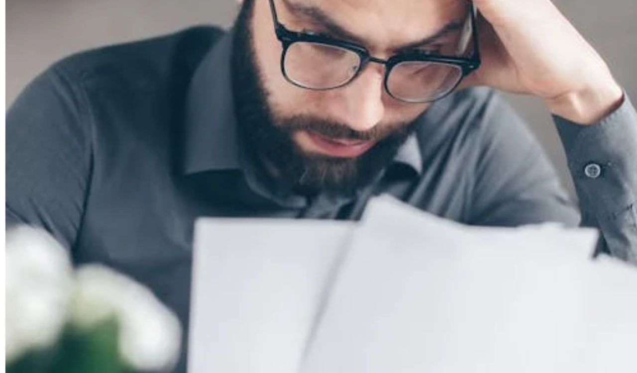 Worried man reading documents at a table, representing unexpected travel expenses or poor budgeting while planning a trip