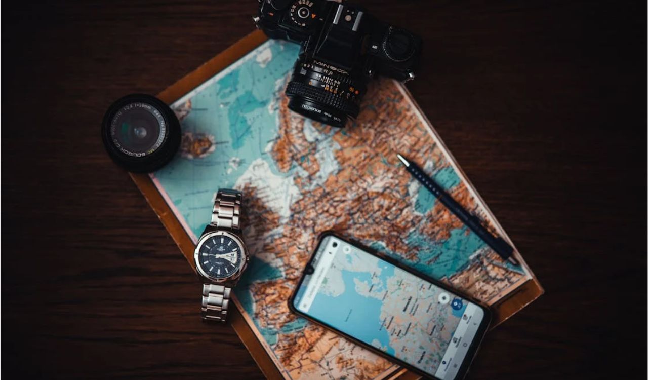 Flat lay of travel essentials including a map, camera, smartwatch, and smartphone with navigation, highlighting the importance of flexible itinerary planning