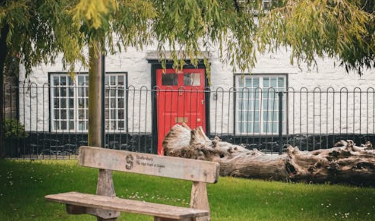 Empty wooden bench in a quiet park with a red door cottage, symbolizing the communication gap when relying only on English abroad