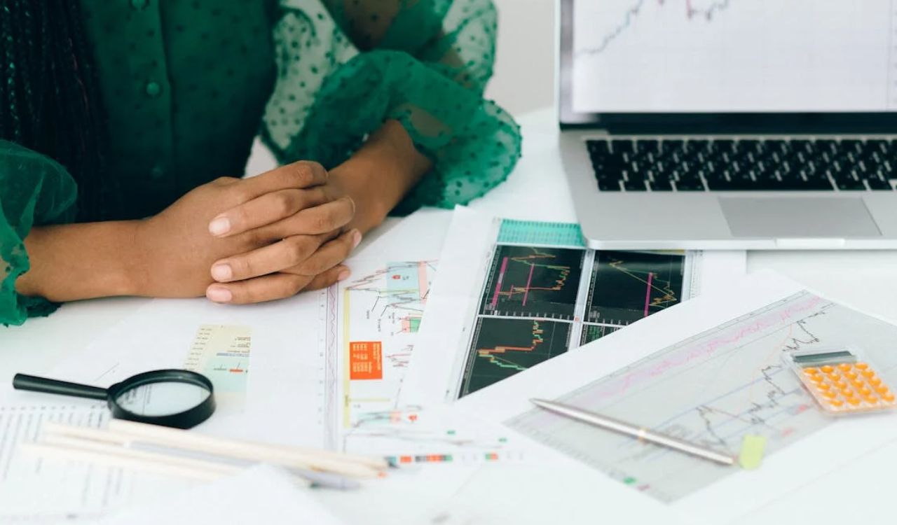 Close-up of a woman in a green dress analyzing financial graphs and stock charts on paper and laptop, emphasizing smart travel budgeting