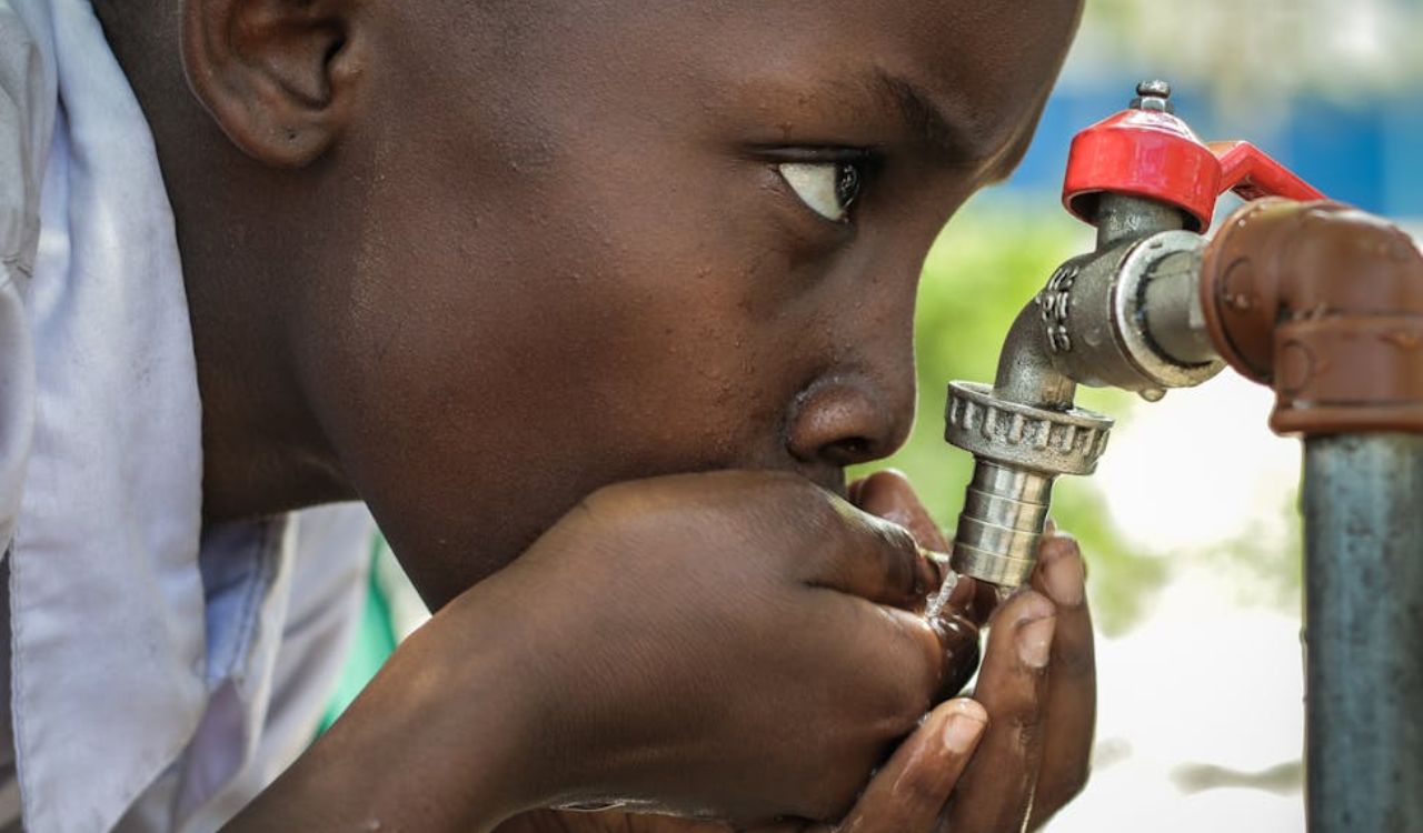 Young boy drinking water directly from a metal outdoor tap, highlighting the importance of checking water safety when traveling