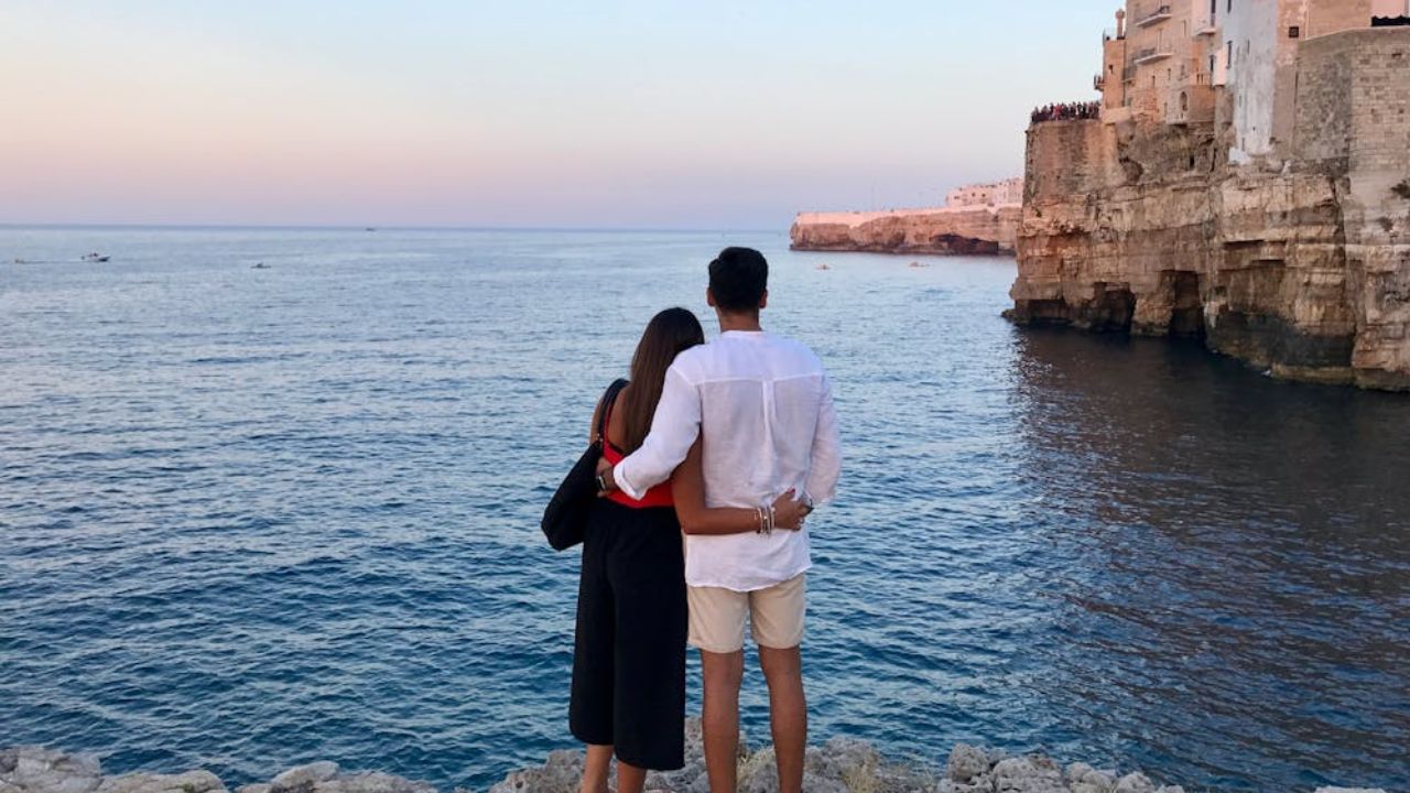 A couple standing on a rocky shore, overlooking the ocean during sunset