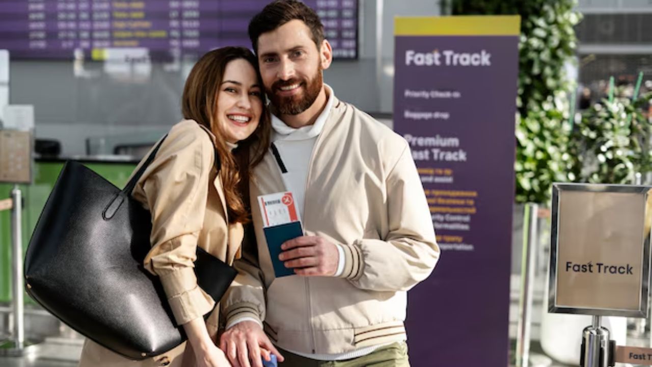 A couple smiles at the airport, holding travel documents in front of a "Fast Track" sign