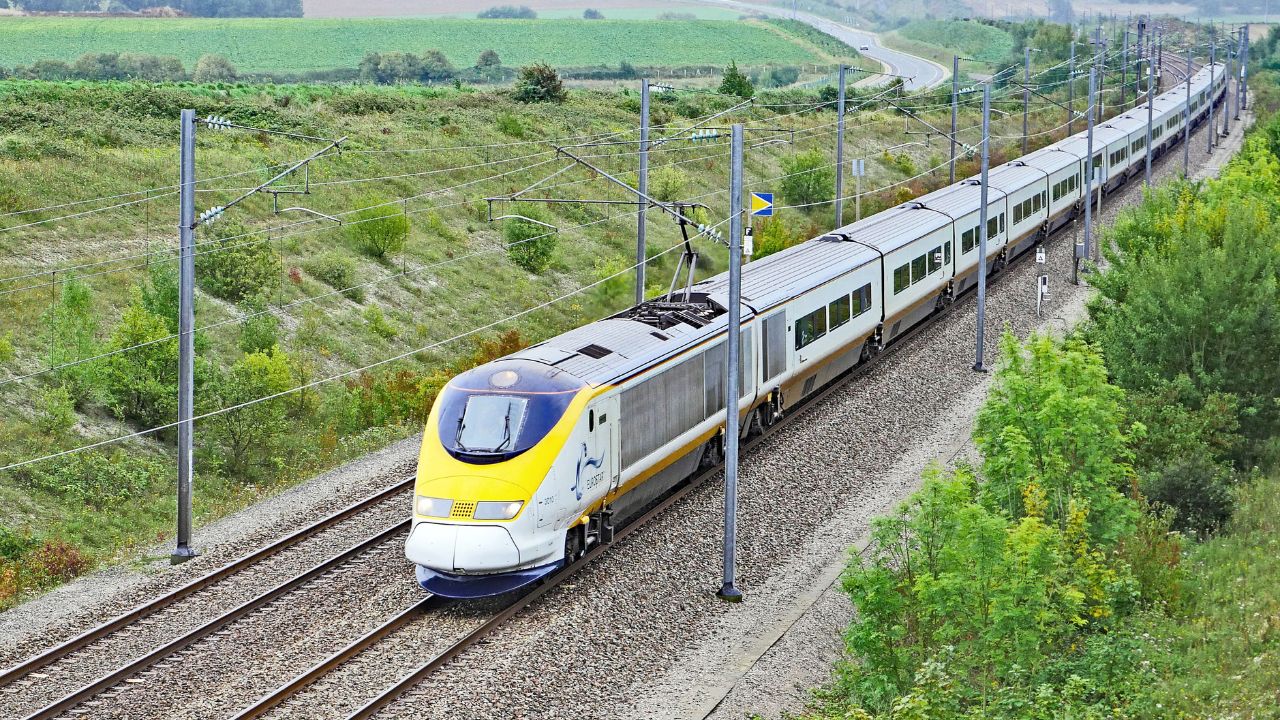 High-speed passenger train traveling through a rural landscape with green fields and power lines.