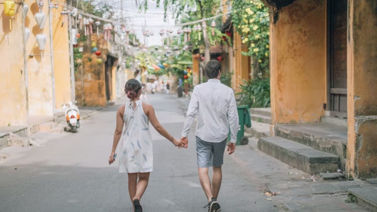 Couple holding hands while strolling through a charming, lantern-lined street.