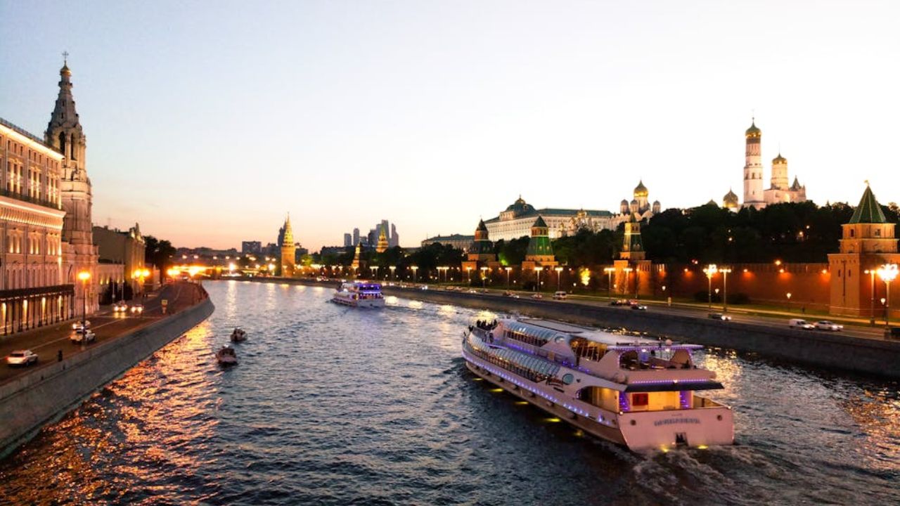 Illuminated river cruise boat sailing through Moscow at sunset with the Kremlin in the background.