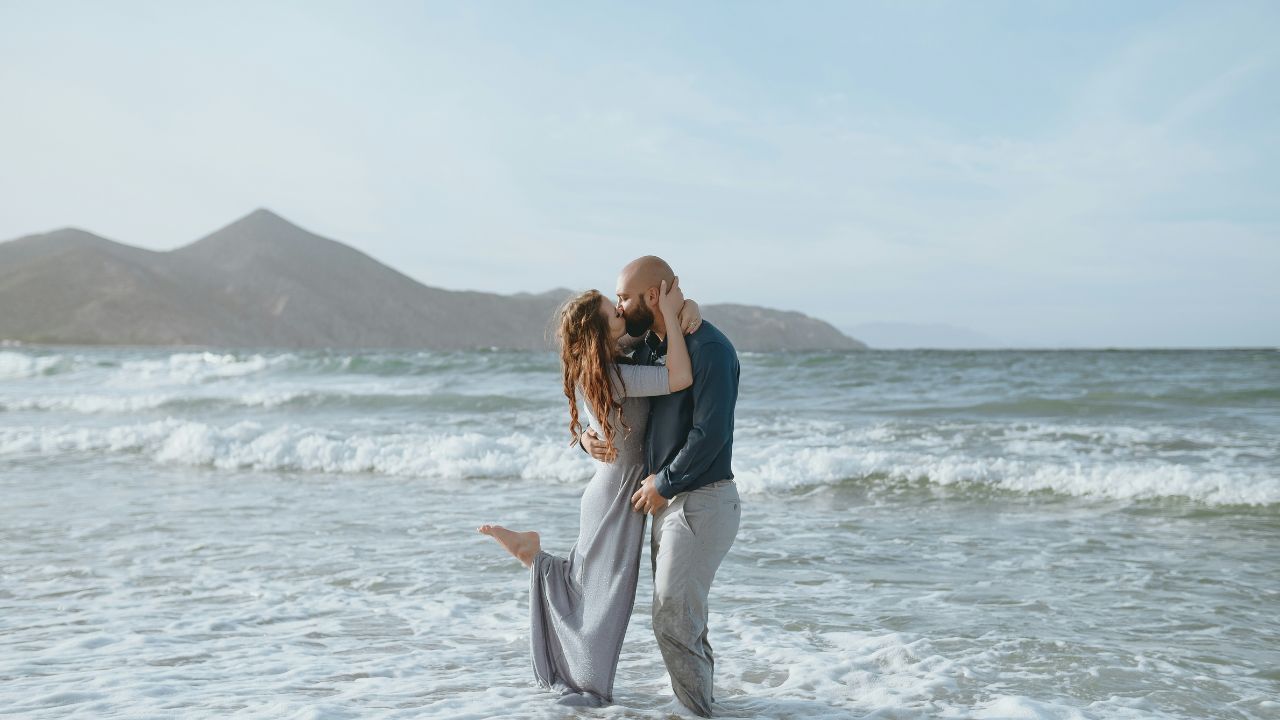 Couple embracing and kissing in the ocean with mountains in the background.