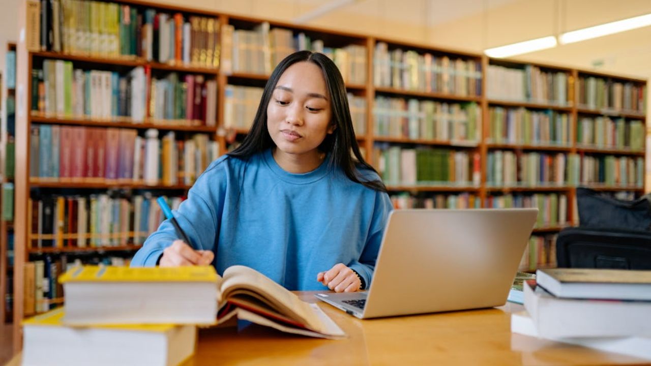 Student studying in a library with books and a laptop.