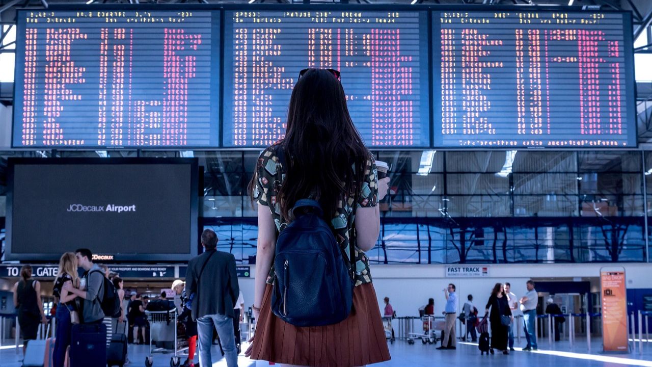 Woman with backpack looking at flight departure board in airport terminal.
