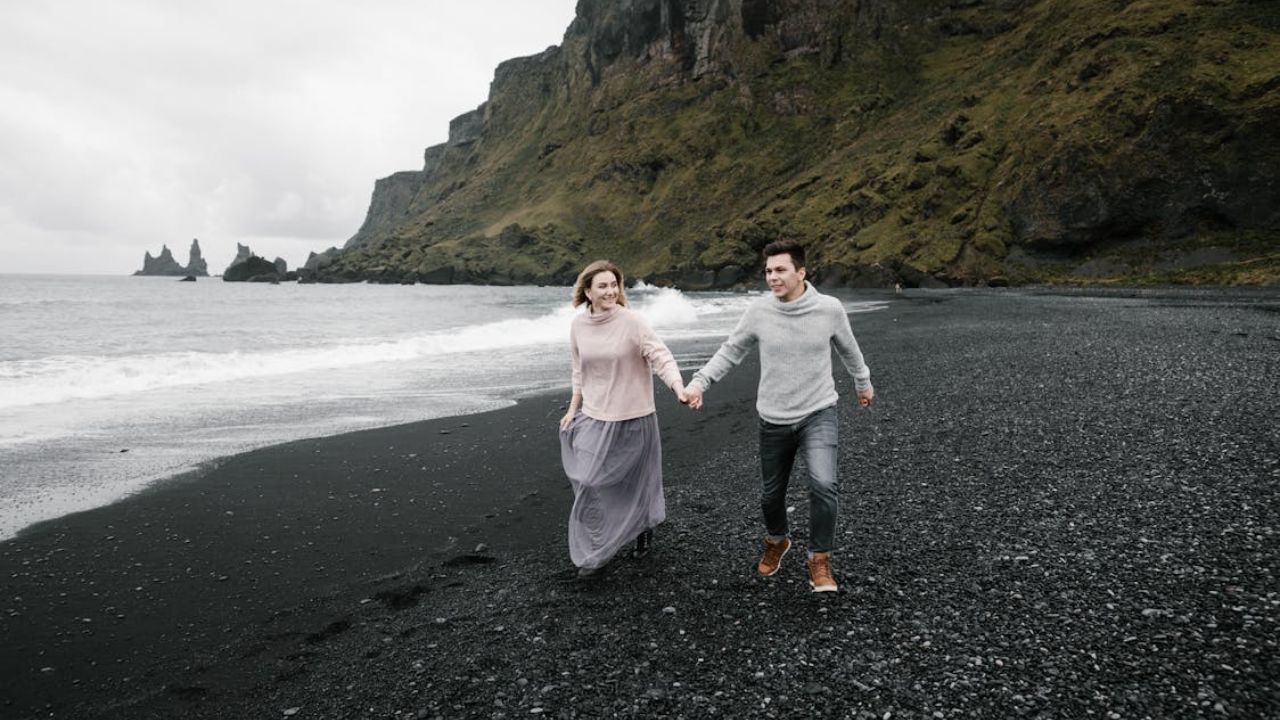 Happy couple walking hand-in-hand on a black sand beach in Iceland