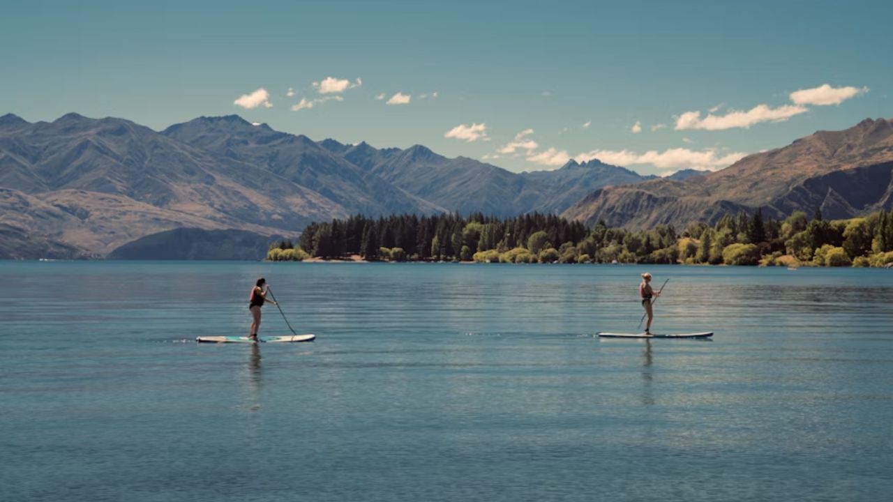 Two paddleboarders float on a calm lake with majestic mountains in the background.