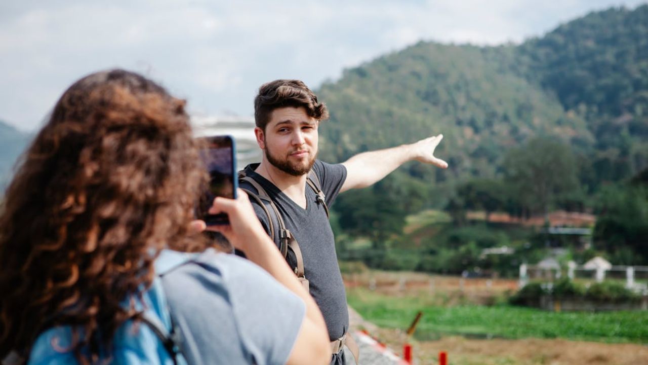 Man pointing at mountain landscape while woman takes his photo.