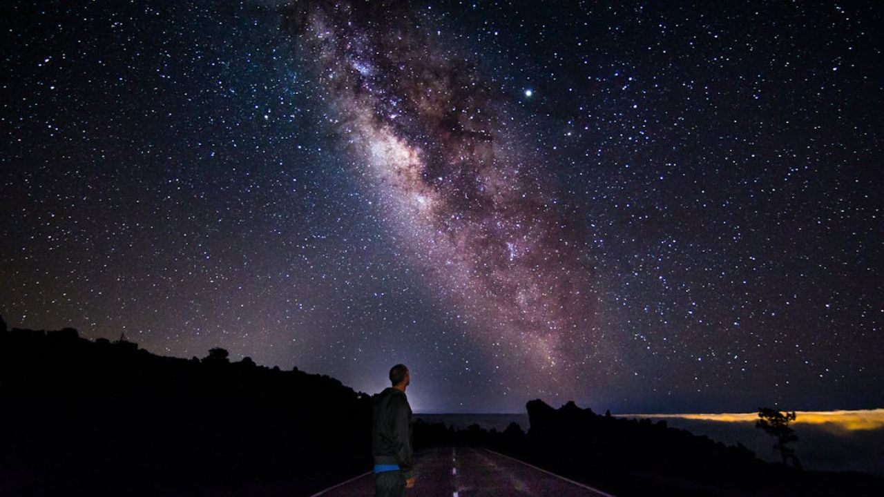 A man stands on an empty road, gazing up at the dazzling Milky Way.