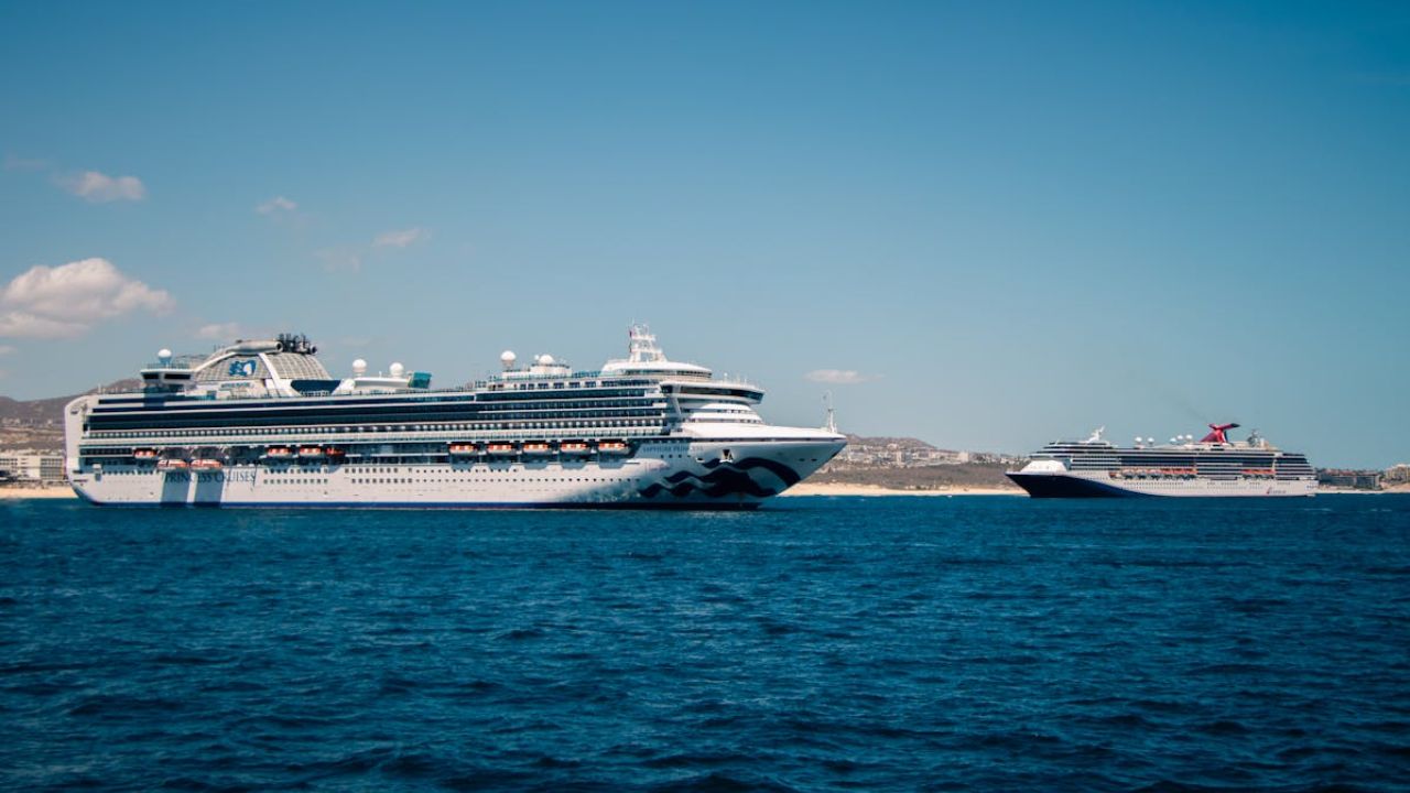Two large cruise ships sailing on blue ocean near a coastal city.