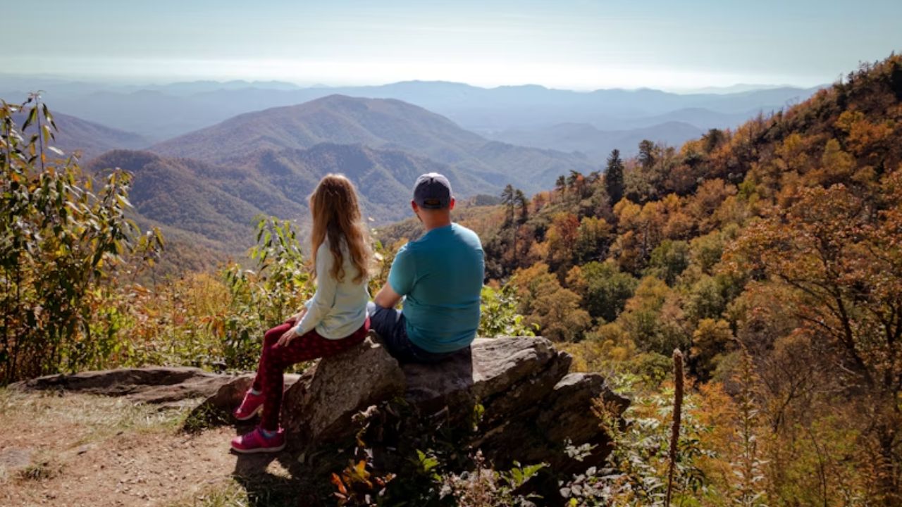 Couple sitting on a rock, admiring scenic mountain views in the Blue Ridge Mountains during fall.