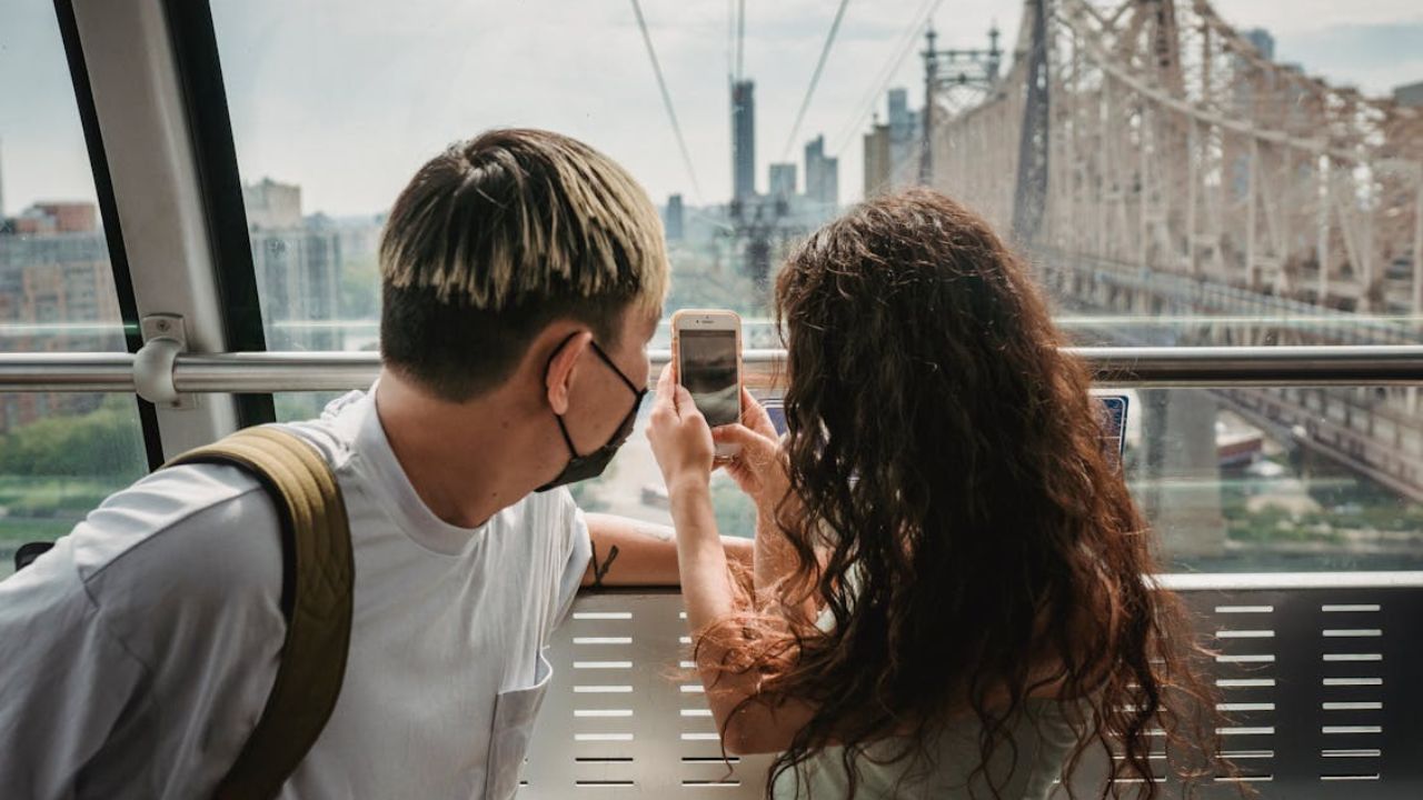 Couple taking a photo while riding a tram with a city bridge view