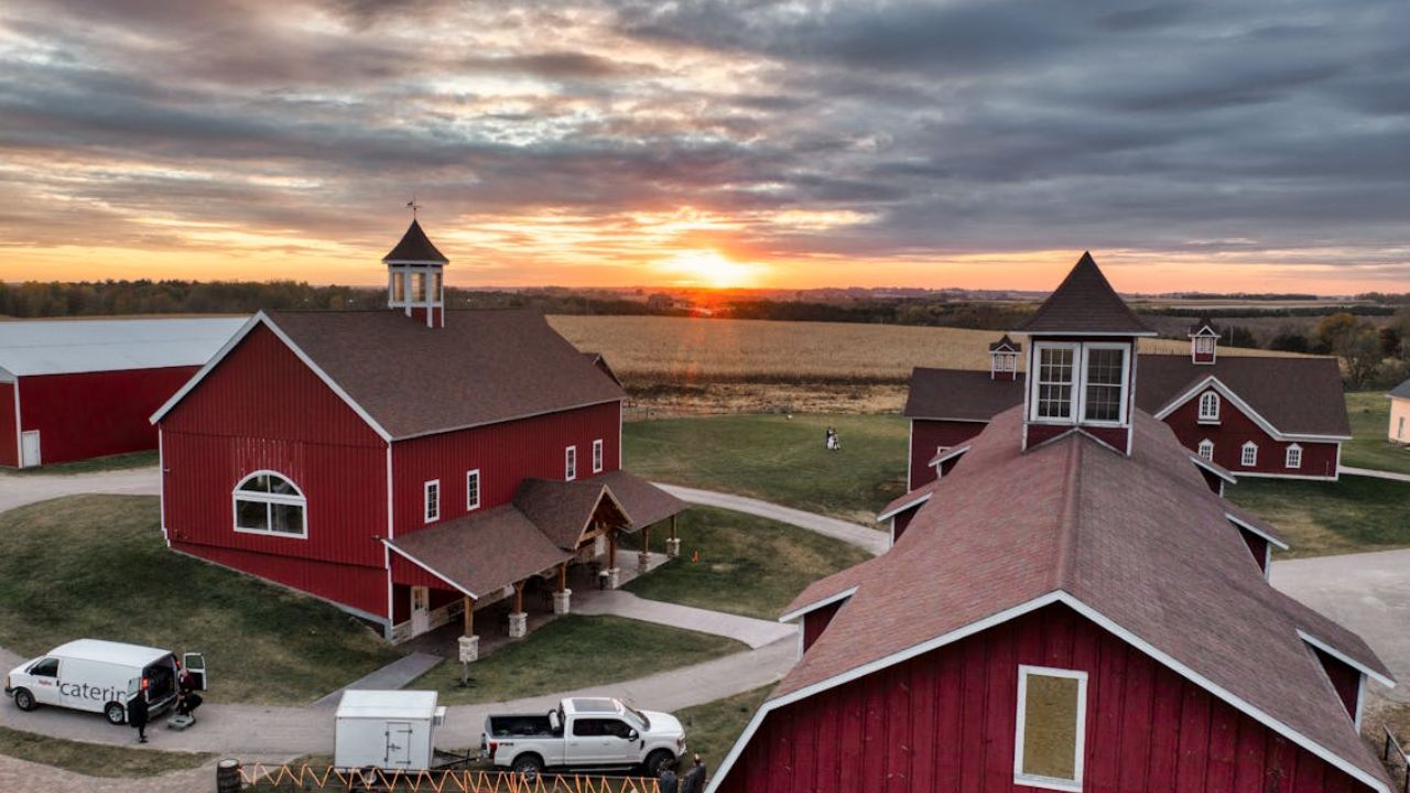 Red barns on a rural farm at sunset with cloudy sky and surrounding fields.